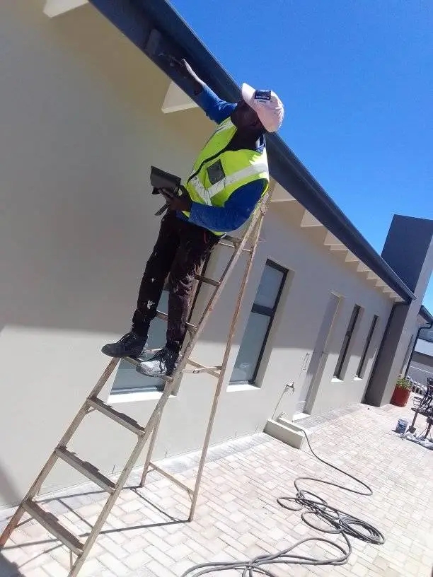 Painter on a ladder finishing the eaves and gutter line of a home