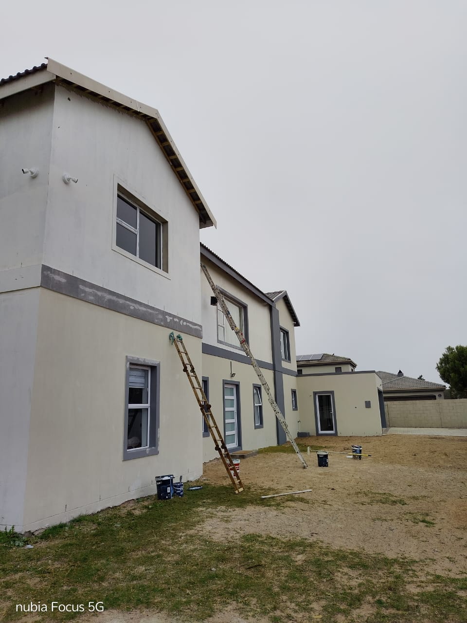 Exterior house repaint in progress with ladders against a double-storey wall